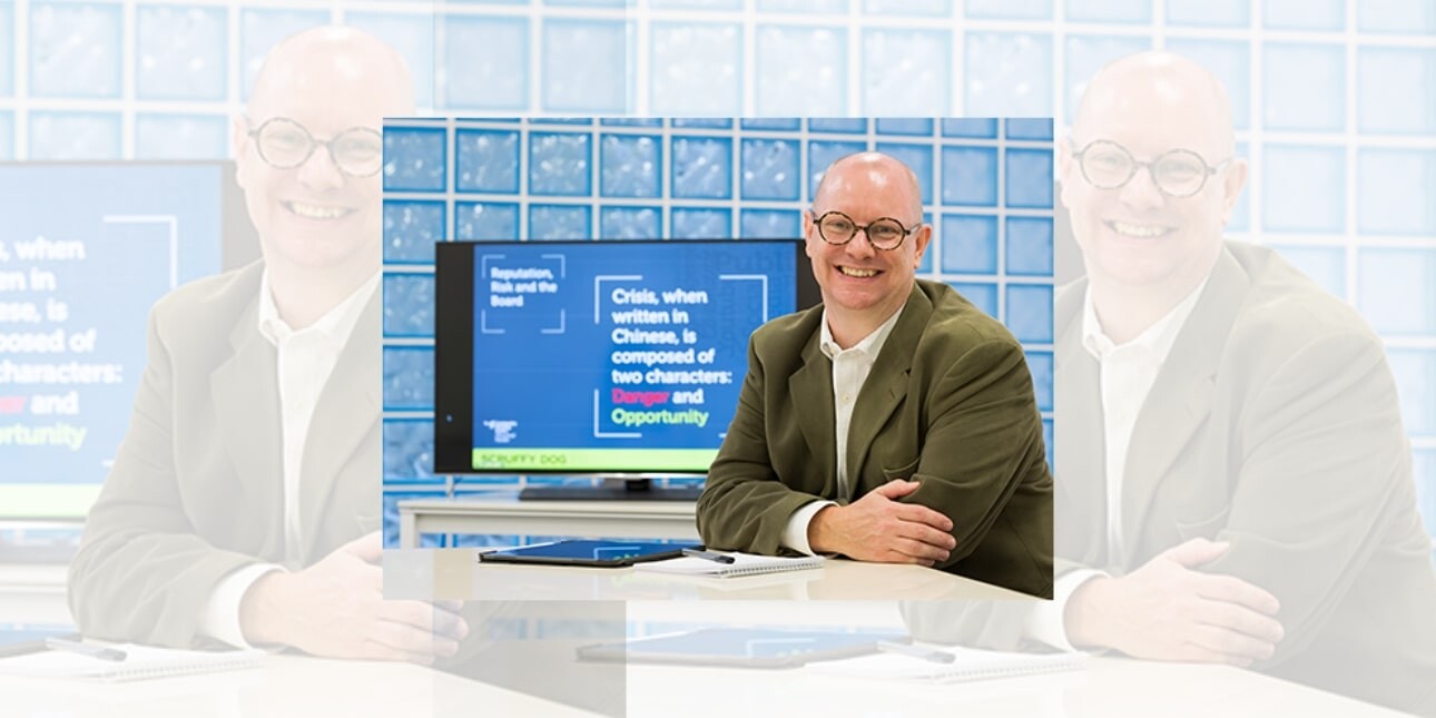 A tryptic of John Wilkinson sat at a desk with a monitor next to him and glass brick wall behind. John is a white man with bald head and glasses. He wears a khaki jacket and white shirt