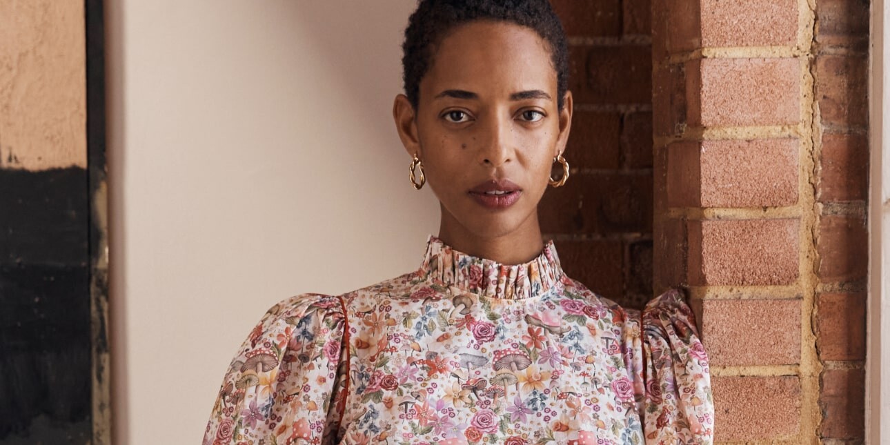 A Black female model wearing a floral dress. The background is bare brick and white walls