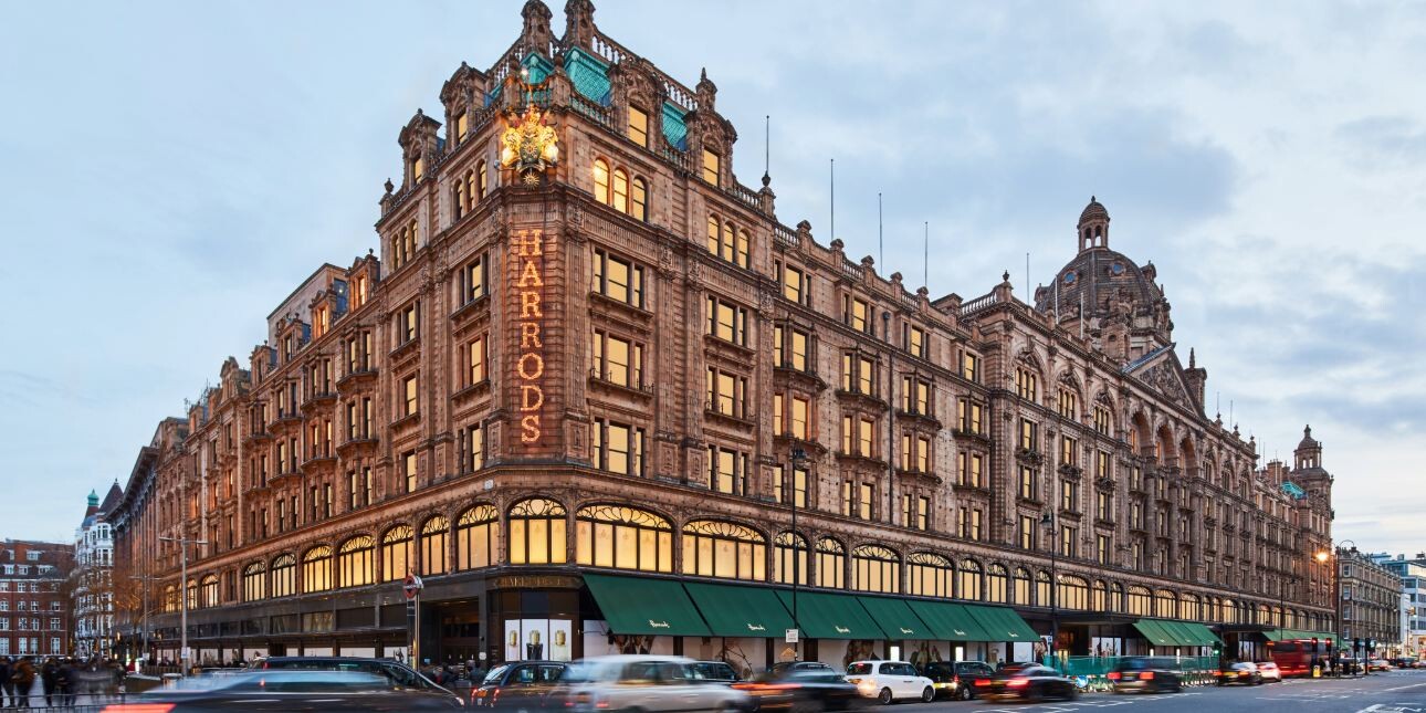 The grand, terracotta-clad Harrods exterior with a blend of Victorian and Beaux-Arts architectural styles, green awnings above the ground floor and Harrods sign on the corner.