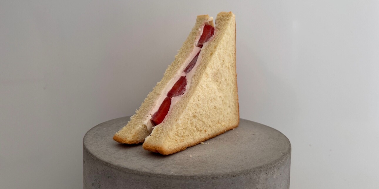An image of the M&S red diamond strawberry and creme sandwich on a cylindrical grey stone plinth. The background is grey.