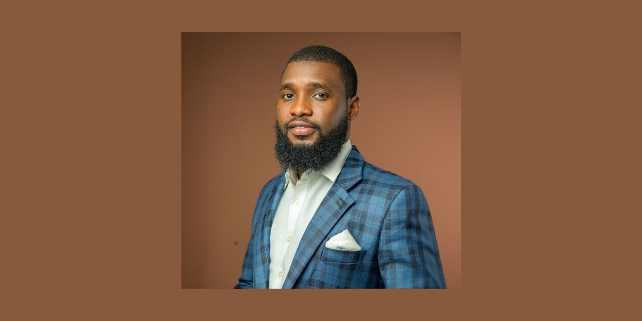 On a brown background, a colour portrait of David Olajide wearing a blue check suit jacket. David is a Black man with dark hair and beard. He is looking side on to the camera.