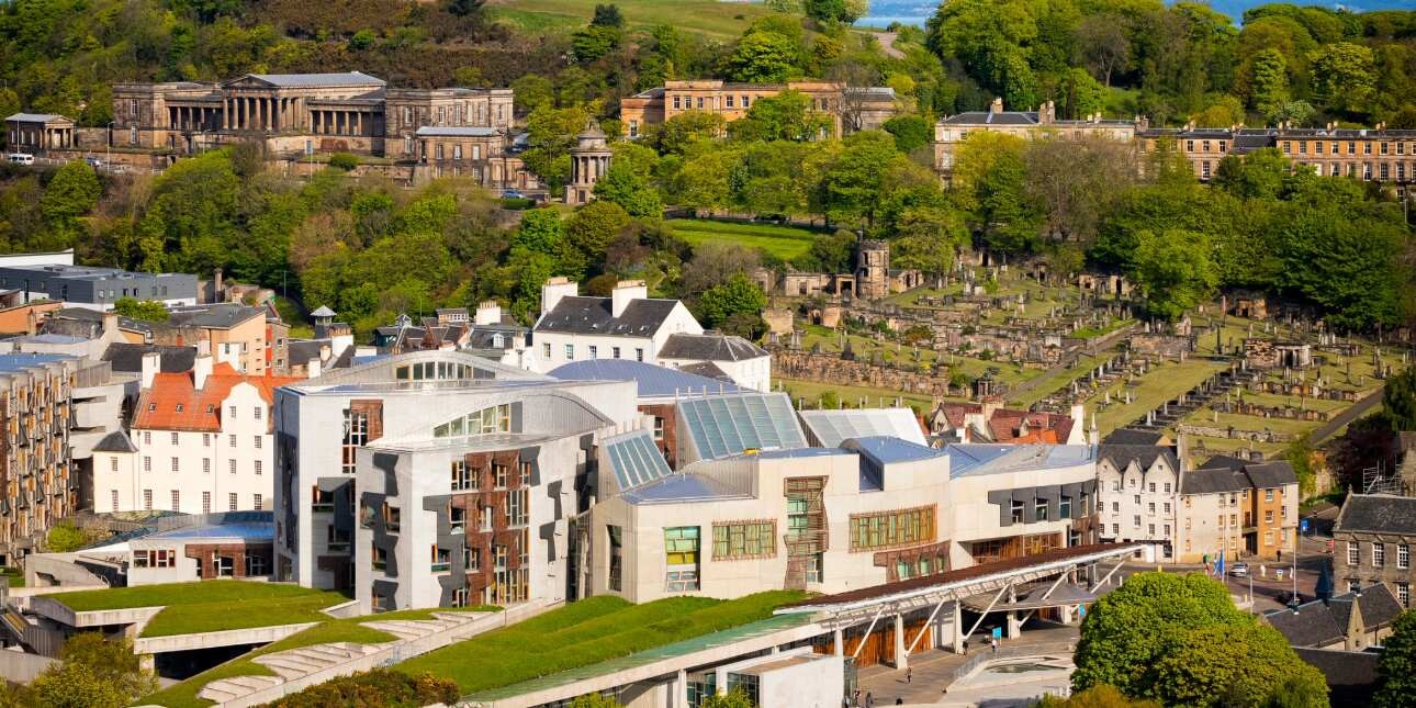 An aerial photograph with the modern Scottish parliament in the foreground and other historic buildings among the greenery in the background