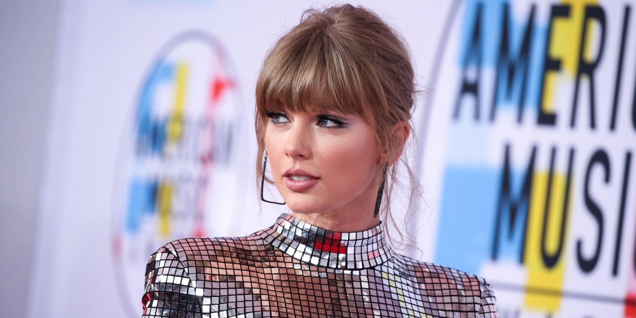 A portrait of Taylor Swift at an event look off camera. She is white with long blond hair and wears a silver sparkly dress.