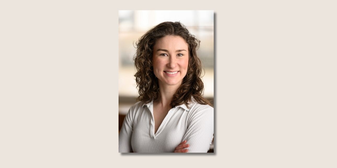 A colour portrait of Zenia Duell. Zenia is a white woman with long, dark curly hair who is looking at the camera and smiling