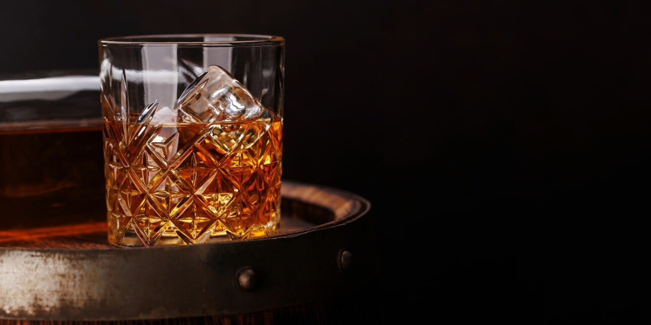 On a black background a glass of whisky stood on the top of an aged barrel.