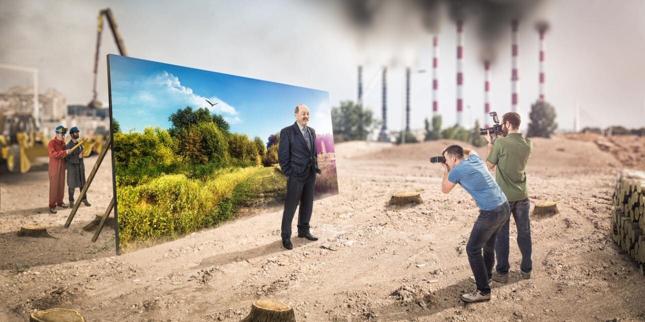 A computer generated image of a businessman in a suit posing for photographs while stood in front of a screen showing trees and nature. Around him are tree trunks, scorched earth, construction and smoking chimneys