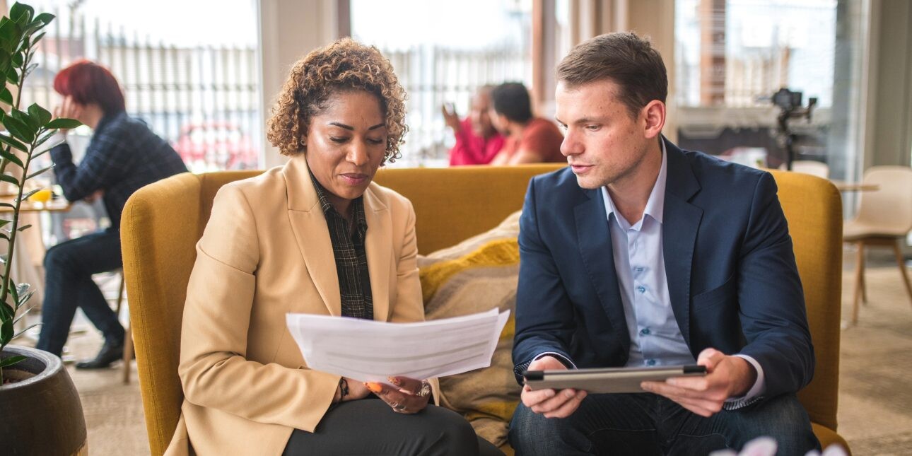 Two colleagues sat on a yellow sofa discussing paperwork