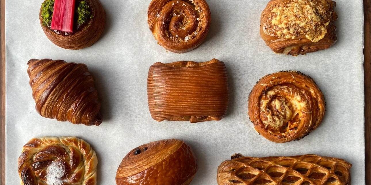A bird's eye photograph of nine different types of croissant lying on a sheet of greaseproof paper
