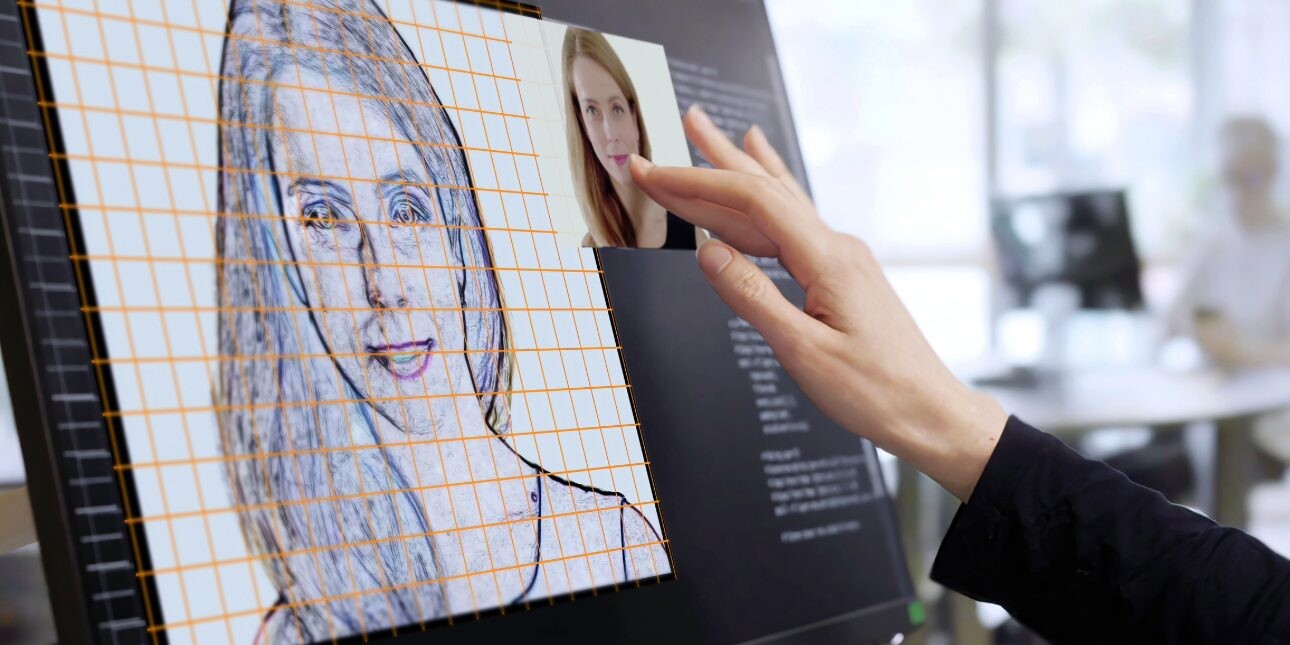 A woman’s hand working on a computer touchscreen. She’s working on an AI virtual model of a young woman.