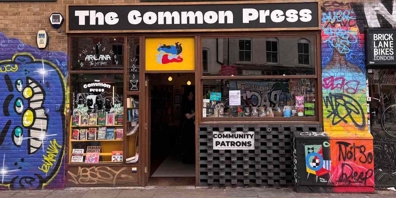 The exterior of the Common Press bookshop with a large window. The brickwork to the side is covered in colourful graffiti.