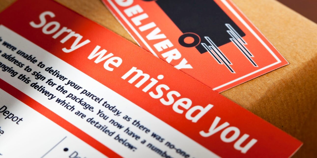 A red missed delivery card placed on top of a cardboard box that features a delivery sticker.