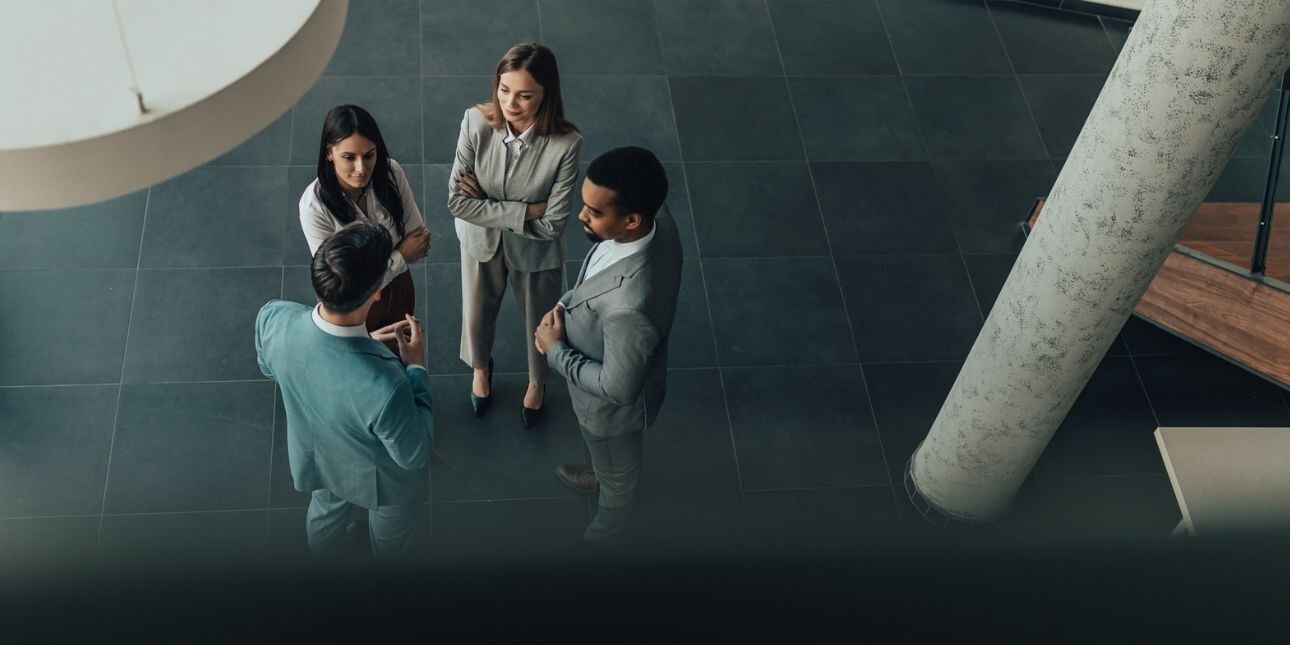 An overhead shot of four professional business people stood in discussion in a modern office.