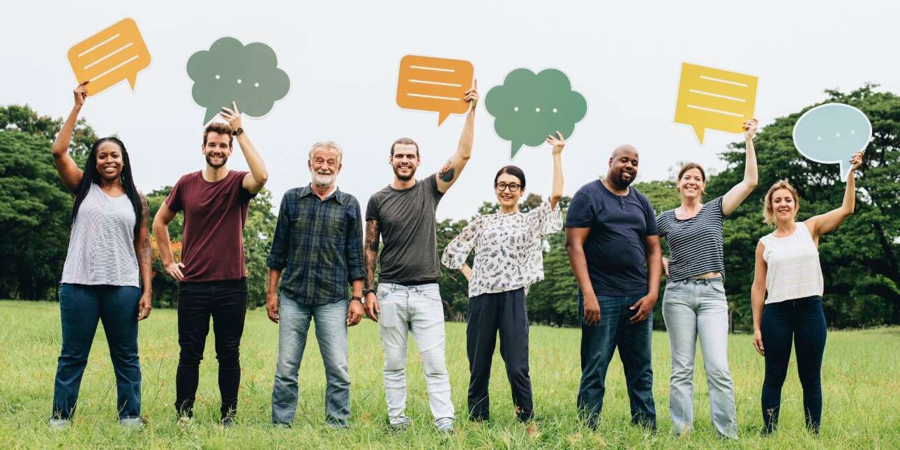 Eight people of different ages, genders and ethnicities stood on grass while holding cut out speech bubbles