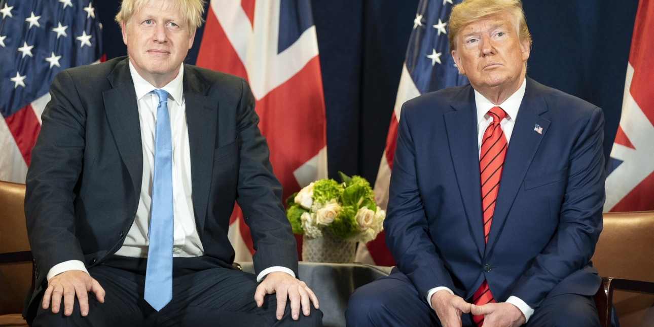 Boris Johnson and Donald Trump sat on chairs facing the camera. Both wear suits. Behind them are two British flags and two US flags.