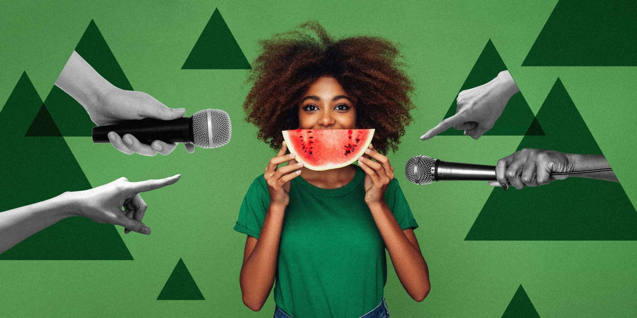 Woman centre of image in green t-shirt holding a slice of melon Infront of her mouth, whilst either side of her there are two hands pointing fingers toward her, and two hands holding microphones toward her.