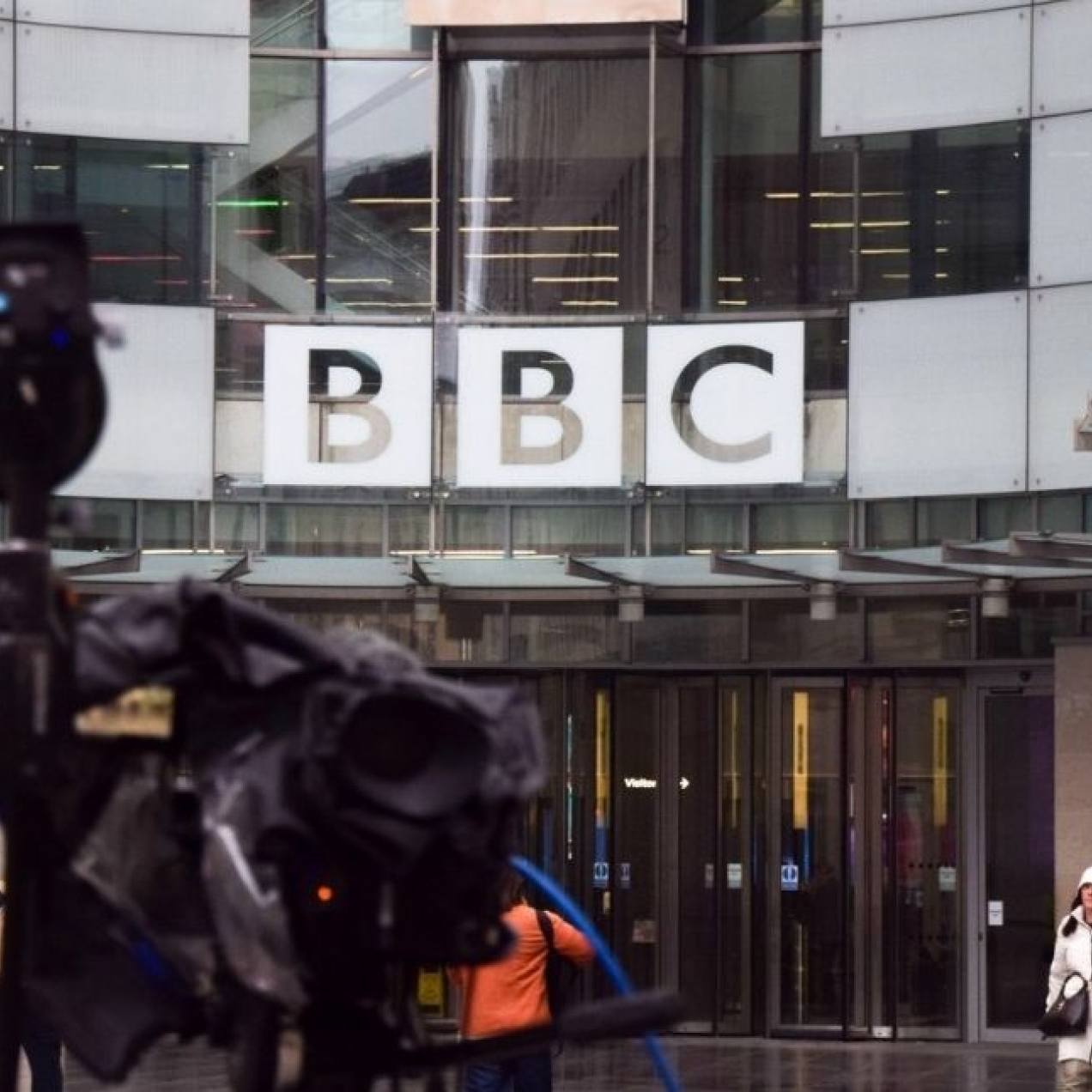 Broadcasting equipment and reporters outside the glass fronted Broadcasting House. The BBC logo is positioned in the background.