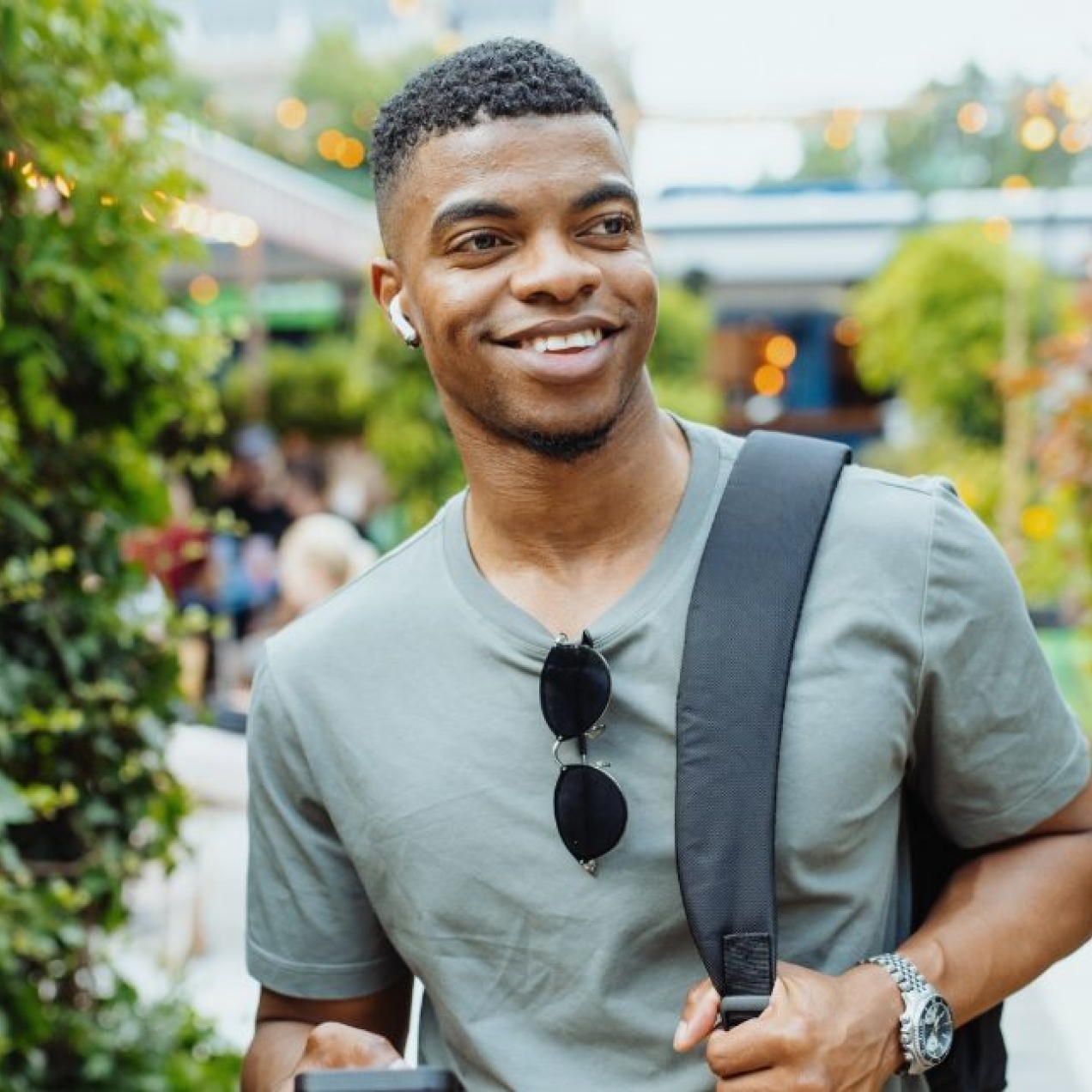 A young smiling Black man wearing earphones and green t-shirts walks in a path surrounded by plants