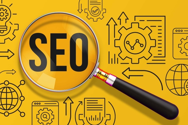 A magnifying glass is placed on a bright yellow background. The letters SEO are within the lens. Alongside are icons of cogs, computer files, arrows and a lightbulb