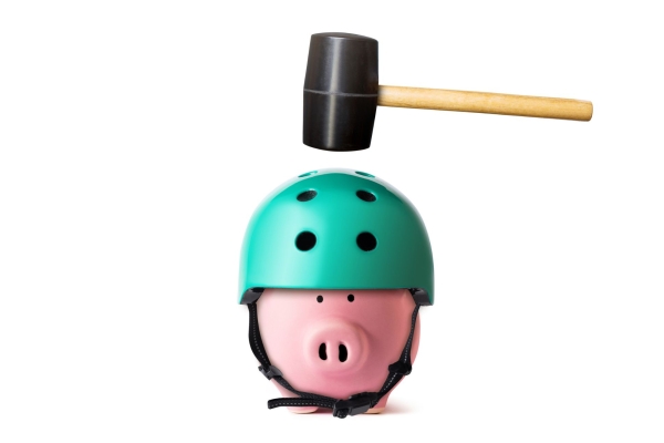A rubber mallet suspended above a pink plastic piggy bank wearing a green cycle helmet