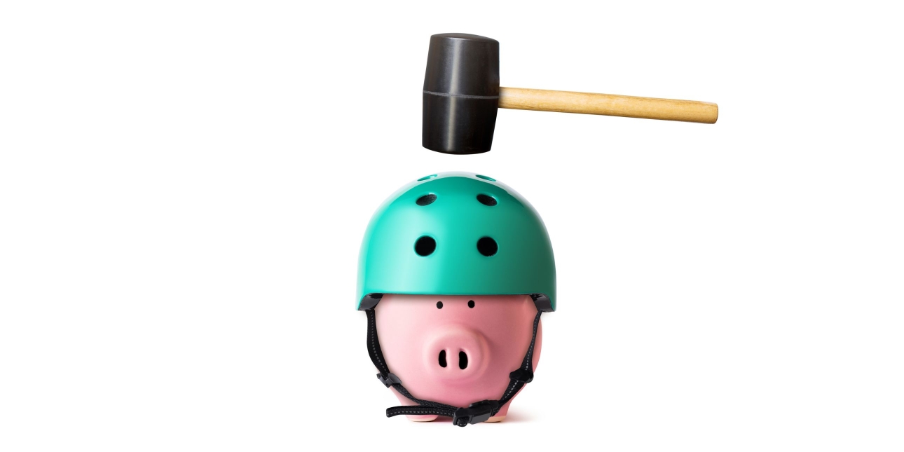 A rubber mallet suspended above a pink plastic piggy bank wearing a green cycle helmet