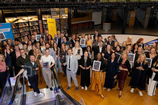 A photograph taken from the top of an escalator of dozens of smiling people holding framed certificates.