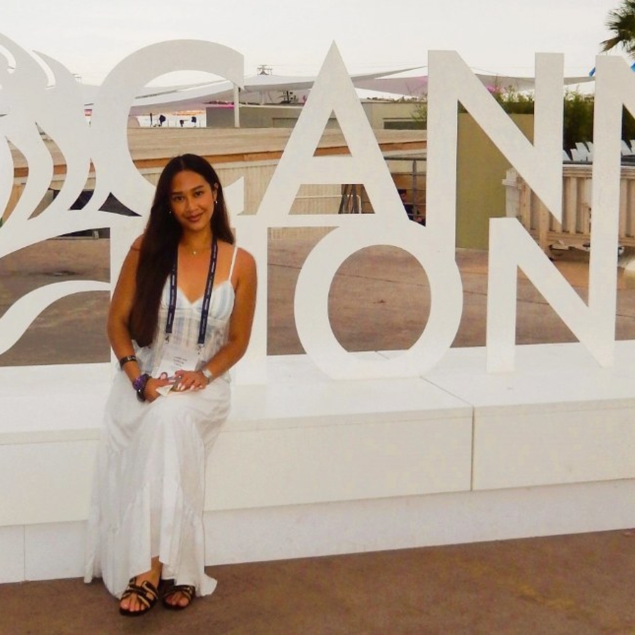 Under a light grey sky Leticia Callista sat in front of a cut out of the words Cannes Lions. In the background are palm trees and assorted conference buildings.
