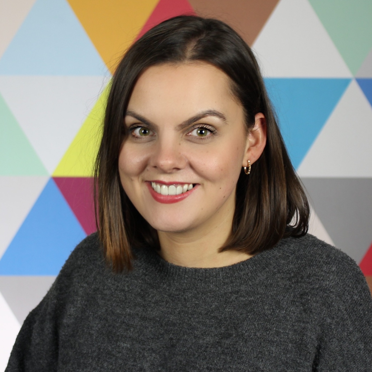 Carly Bannerman, a white woman with dark shoulder length hair, on a background of multicoloured triangles