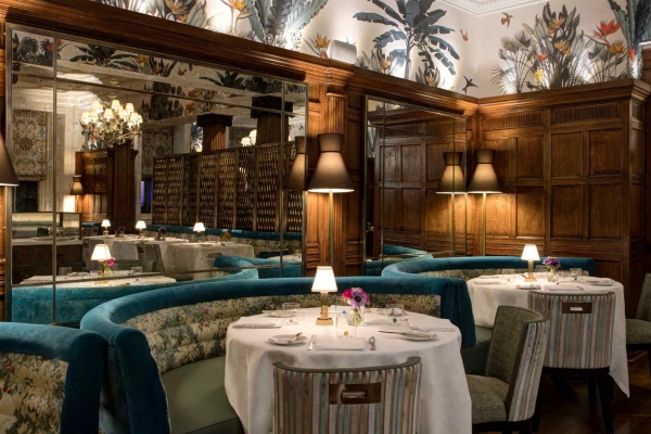 Round tables draped in cloths surrounded by three semi-circular seating benches in turquoise material. Wooden panelling gives a sense of intimacy