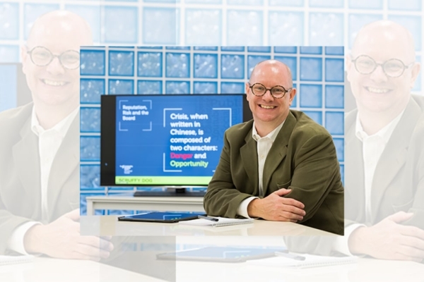 A tryptic of John Wilkinson sat at a desk with a monitor next to him and glass brick wall behind. John is a white man with bald head and glasses. He wears a khaki jacket and white shirt