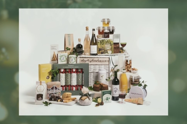 On a green background an image of a Daylesford Christmas wicker hampers surrounded by an assortments of food