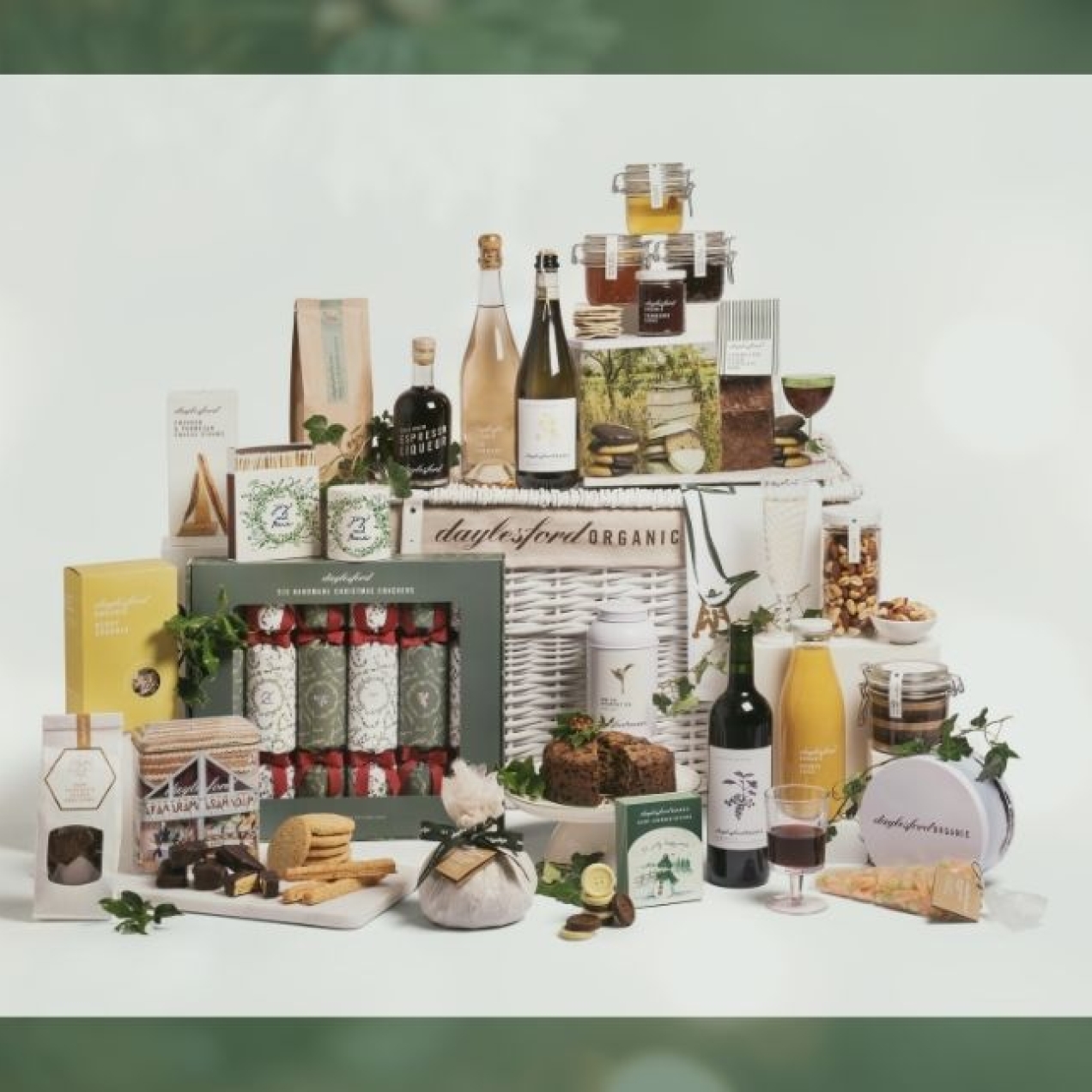 On a green background an image of a Daylesford Christmas wicker hampers surrounded by an assortments of food
