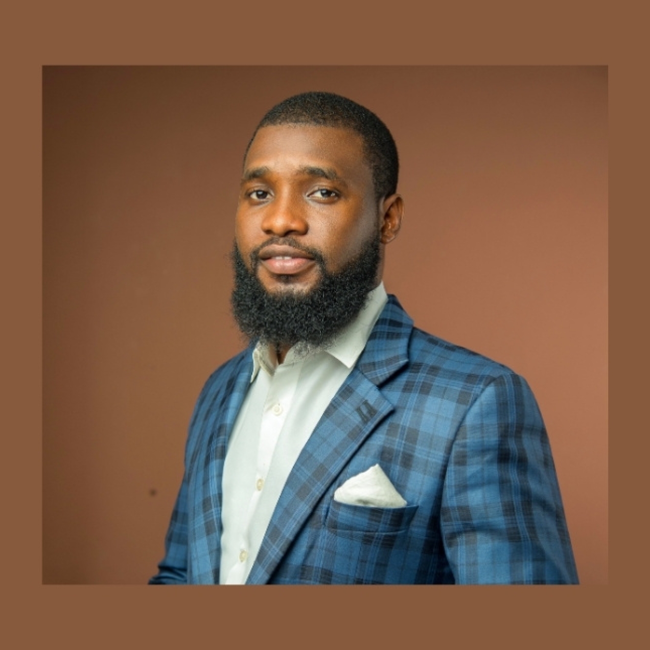 On a brown background, a colour portrait of David Olajide wearing a blue check suit jacket. David is a Black man with dark hair and beard. He is looking side on to the camera.
