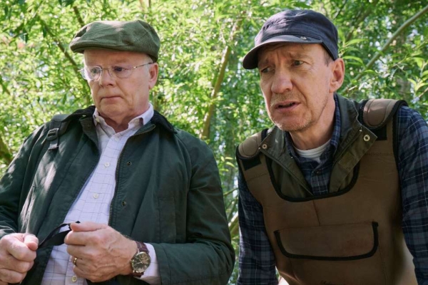 Against a backdrop of leafy trees the actors Peter Hammond and Jason Watkins are photographed in character looking at something out of shot.