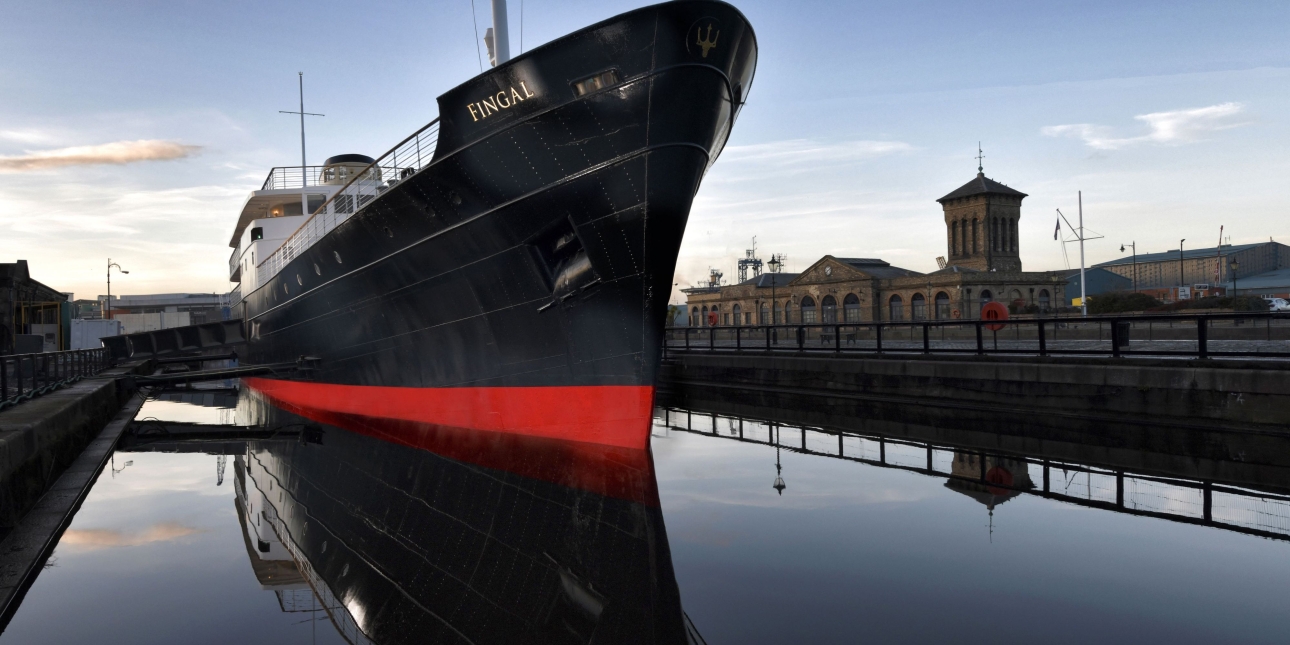 The Fingal in dock at twilight. The bow is painted black with red lower trim and white deck.