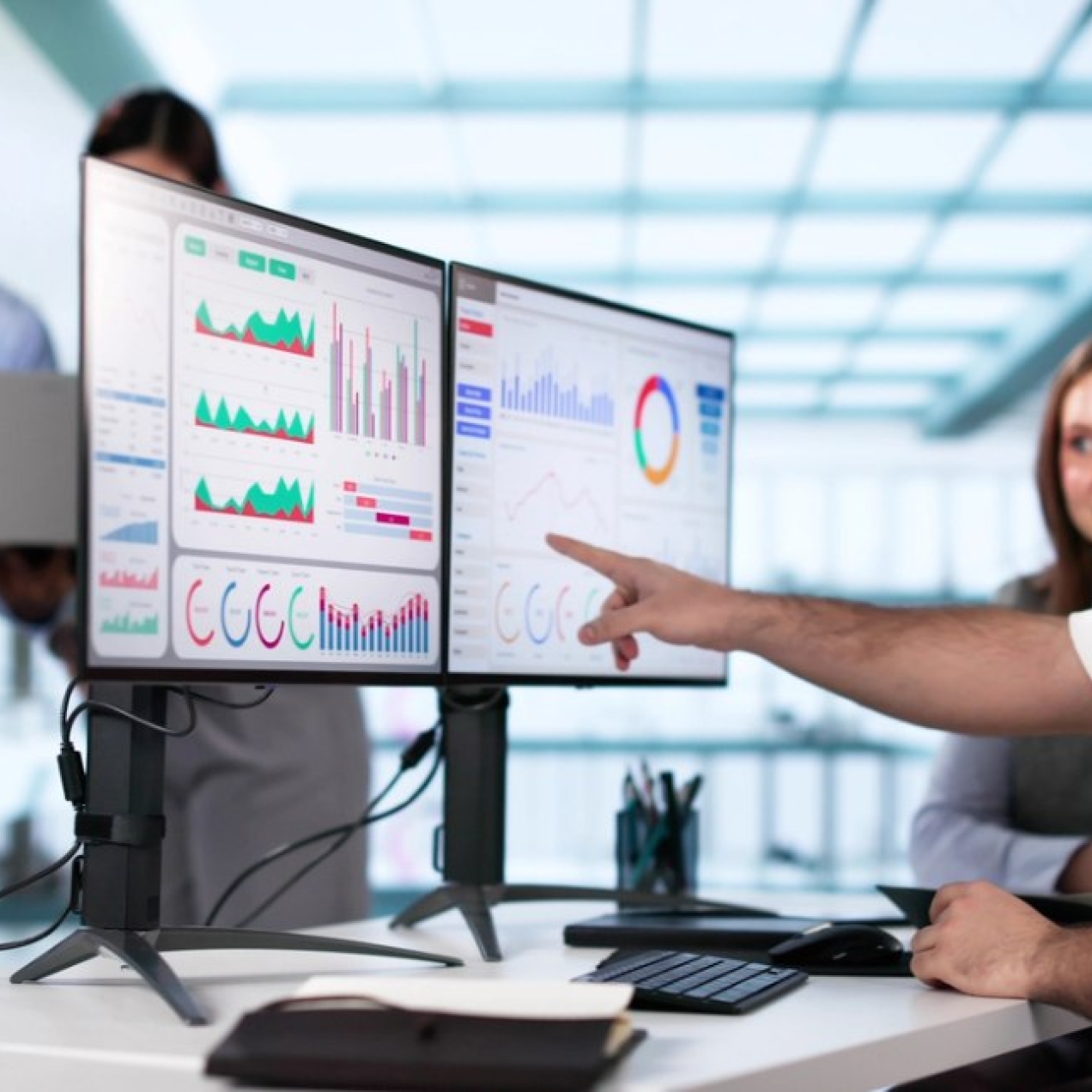 In a modern office a man and woman look at a dashboard on a computer screen while two other colleagues are stood nearby.