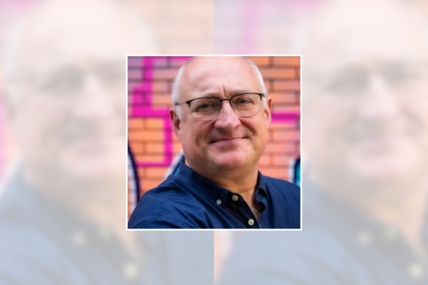 A headshot of Glenn Matchett. Glenn is white man with white receding hair, glasses and wears a dark blue shirt
