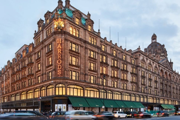 The grand, terracotta-clad Harrods exterior with a blend of Victorian and Beaux-Arts architectural styles, green awnings above the ground floor and Harrods sign on the corner.
