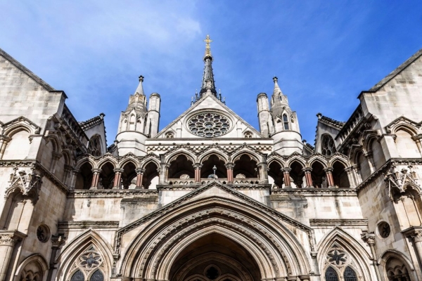 The symmetrical stone facade of the Royal Courts of Justice featuring an arched central section, towers, turrets and a gable containing a rose window above the entrance. A crest and the building name sit either side of the entrance.
