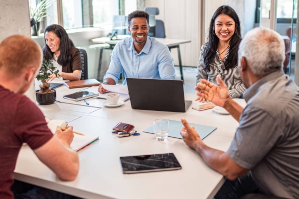 A group of five colleagues of different genders, ages and ethnicities chat around a table: