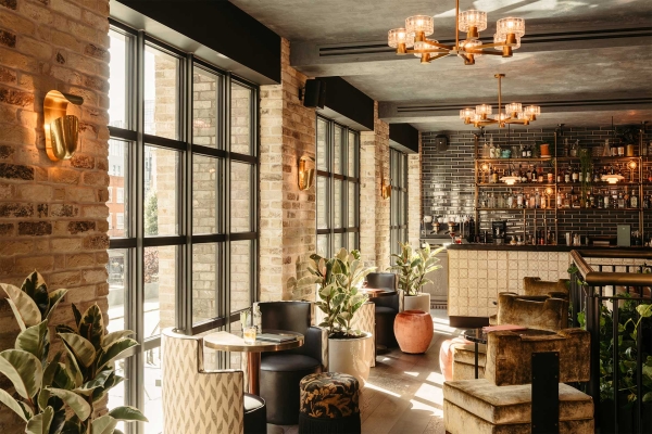 The Hoxton in Southwark - room shows tables and chairs beside a big window plants and lights and a bar in the background