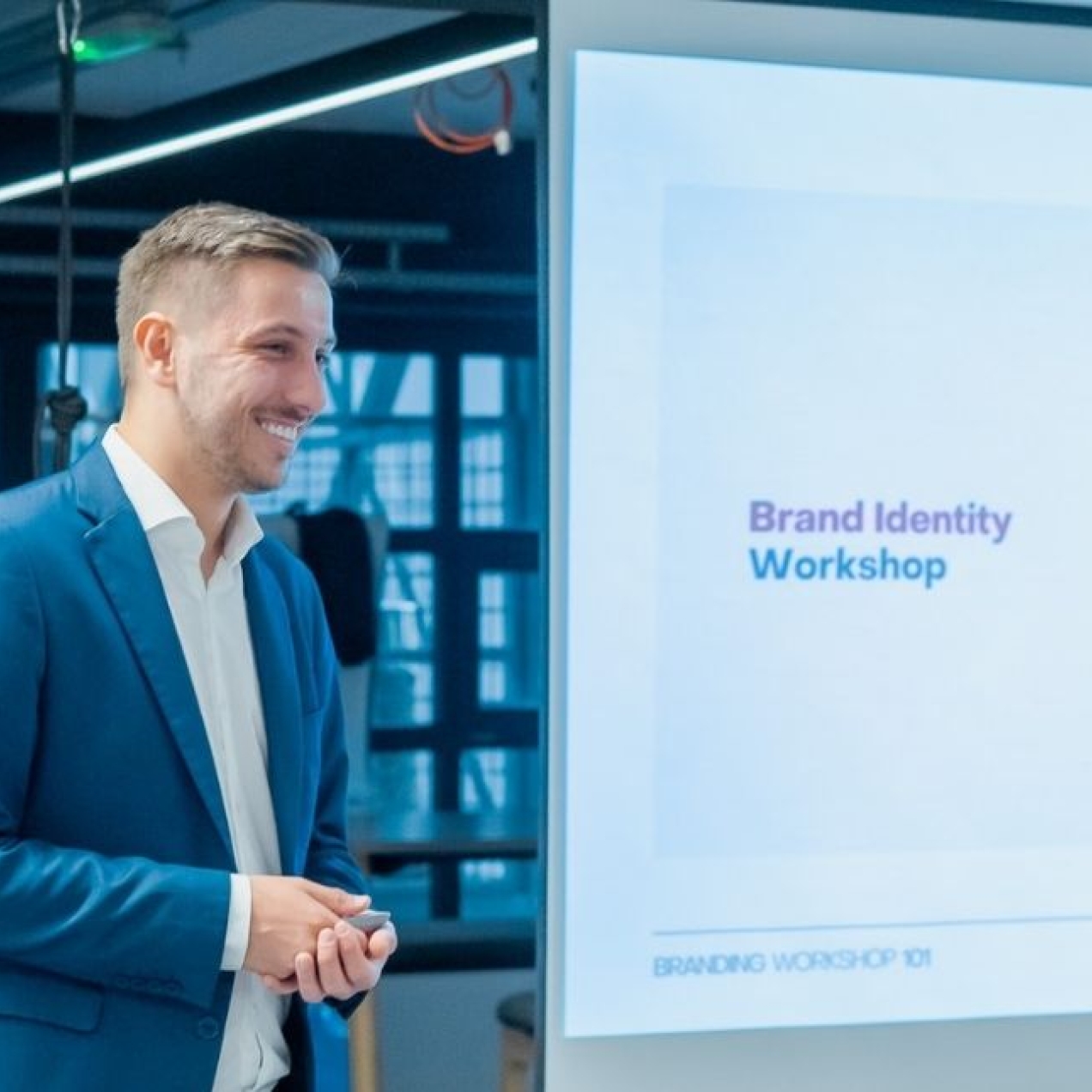 A colour portrait of a smiling Ivan Biošić stood side on to a display board. Ivan is a white man with short blond hair who is wearing a navy suit.