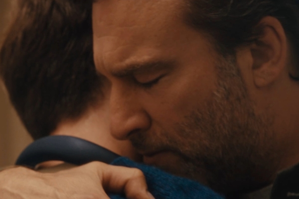 A still from the John Lewis Christmas advert showing a close-up of a white man with dark hair embracing his son, who is also white with dark hair.