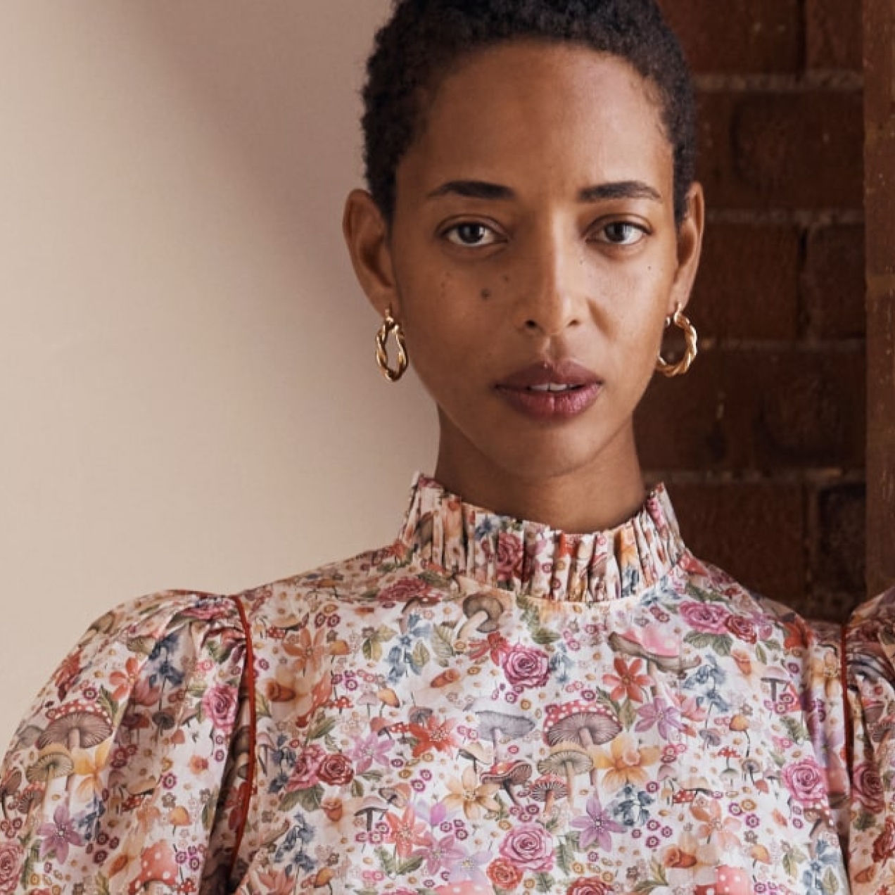 A Black female model wearing a floral dress. The background is bare brick and white walls