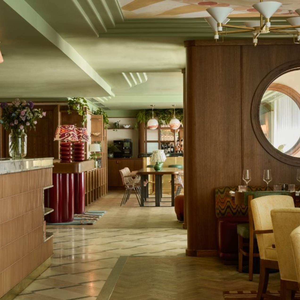 A dining space with pastel coloured bar and lamps, tiled floors, would partition with circular porthole and pistachio coloured decorative ceiling.