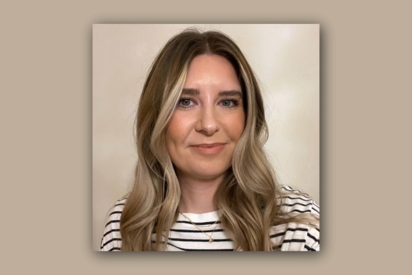 On a fawn background, a square colour portrait of Kat Trinder. Kat is a white woman with shoulder length light brown hair, who wears a white and navy striped top