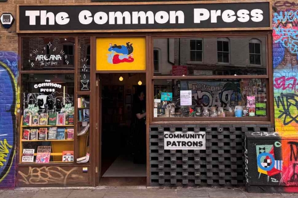 The exterior of the Common Press bookshop with a large window. The brickwork to the side is covered in colourful graffiti.