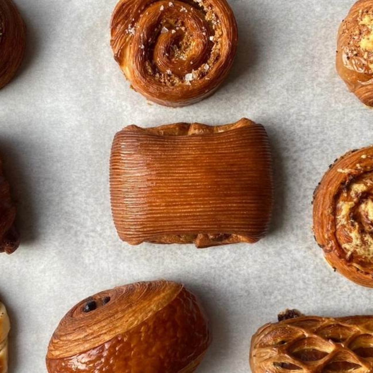 A bird's eye photograph of nine different types of croissant lying on a sheet of greaseproof paper