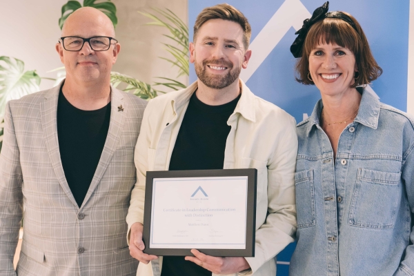 Two white men and one white woman stood smiling in the camera inside an office. The man in the centre is Matt Dunn. He holds a certificate.