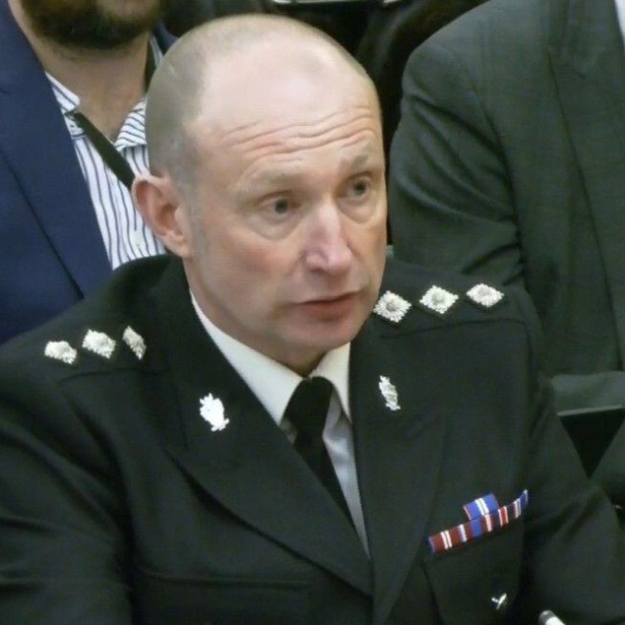 A close up of Mick Wilkinson in black police uniform with other people sat behind him.