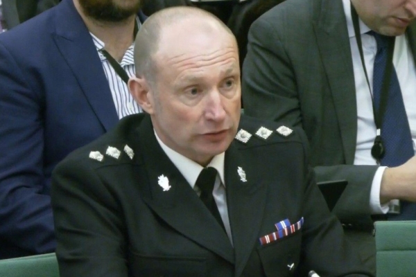 A close up of Mick Wilkinson in black police uniform with other people sat behind him.